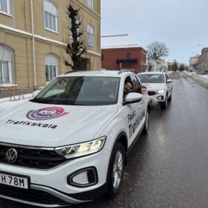 Trafiklärare lutar sig ut genom fönstret på en av Fawaz trafikskolas vita skolbilar på en vintrig gata i Falköping