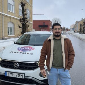 Trafiklärare på Fawaz trafikskola framför skolbilen, en vit VW T-Roc, på en snötäckt gata i Falköping